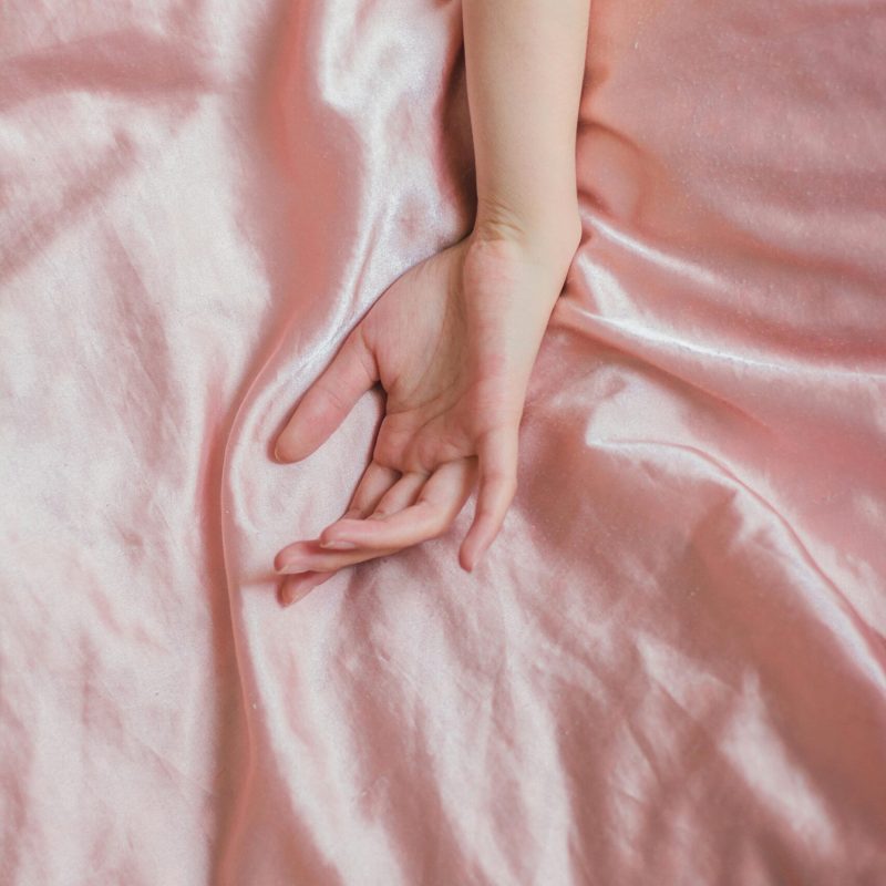 Top view of hand of crop anonymous female on soft silk creased bed sheet at home